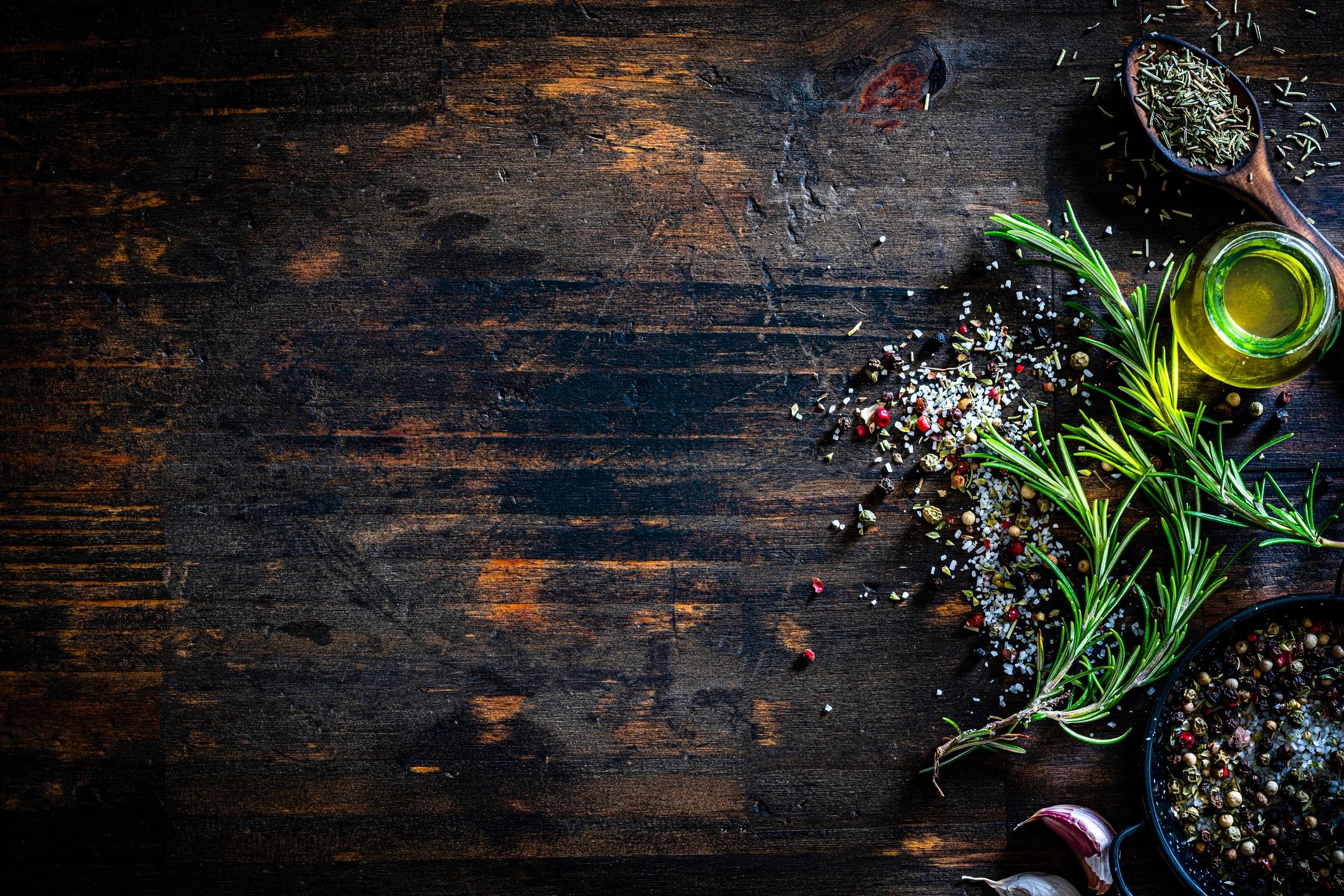 Cooking ingredients like rosemary, salt, pepper, and olive oil on a table